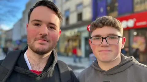 Mason Down (left) and Dylan Steggles are standing side by side, with a busy high street behind them. 