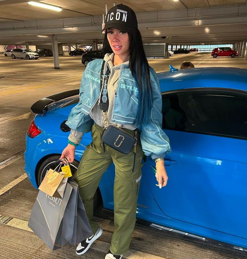 Woman standing next to a blue car holding shopping bags.