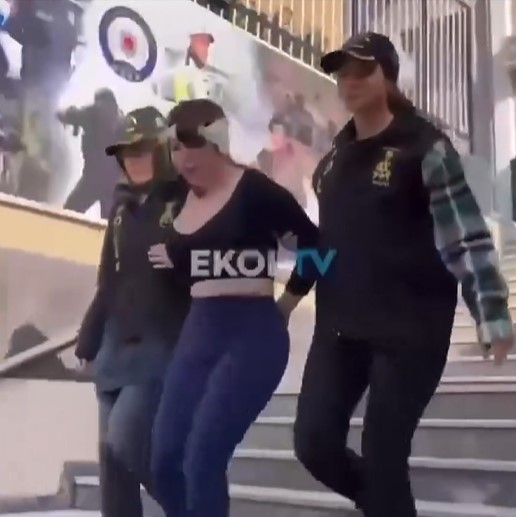 A woman escorted by two officers down some stairs.