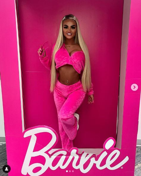 Woman in pink velour tracksuit posing in a Barbie box.