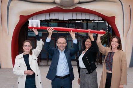 Four people hold up a giant toothbrush as if they’re brushing the teeth of the face at the entrance to Luna Park