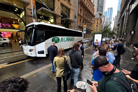 Members of the media stand on the pavement beside the bus